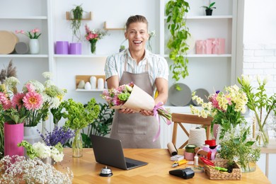 Photo of Professional florist with bouquet of flowers working at wooden table in shop
