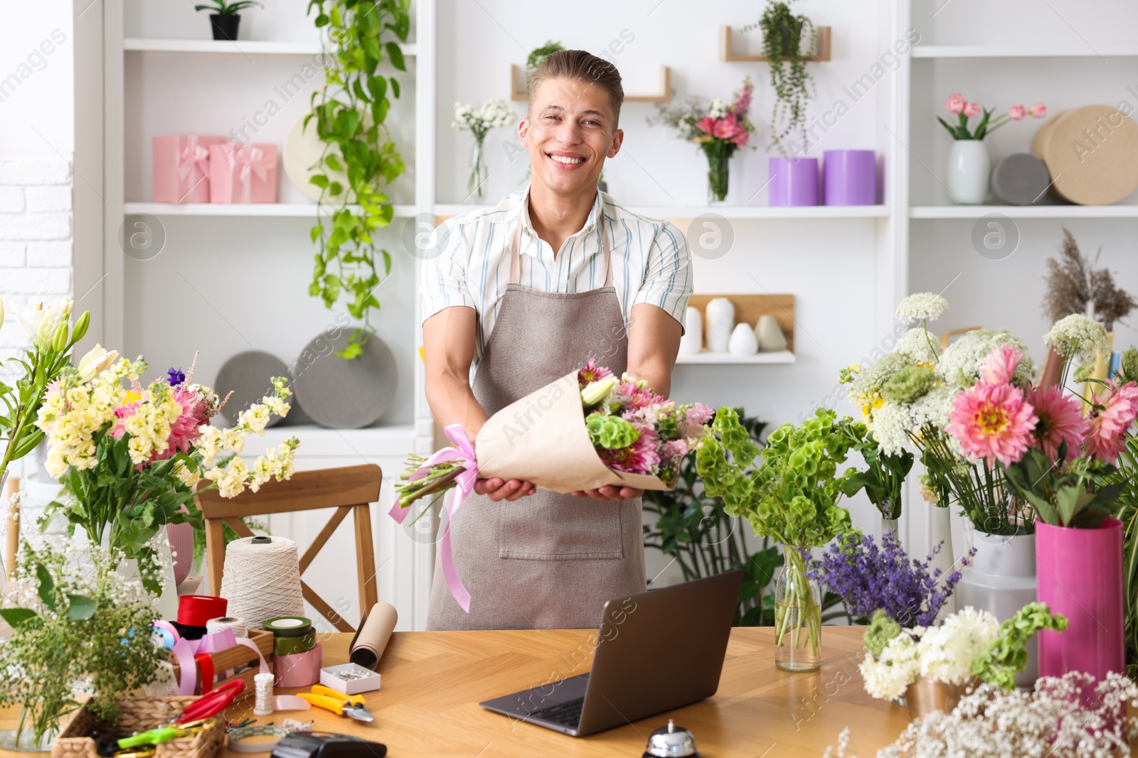 Photo of Professional florist with bouquet of flowers working at wooden table in shop