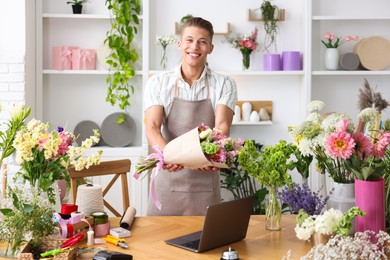 Photo of Professional florist with bouquet of flowers working at wooden table in shop