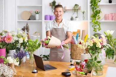 Photo of Professional florist with bouquet of flowers working at wooden table in shop
