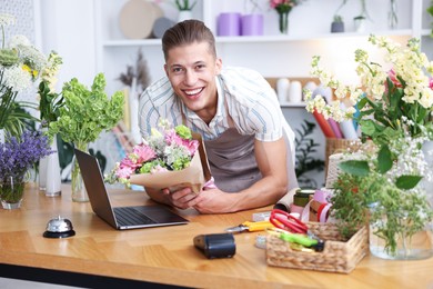 Photo of Professional florist with bouquet of flowers working at wooden table in shop