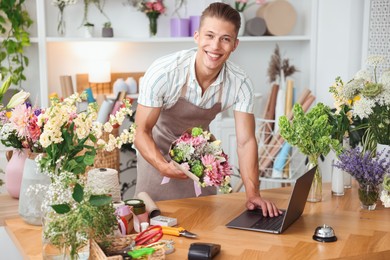 Photo of Professional florist with bouquet of flowers working at wooden table in shop