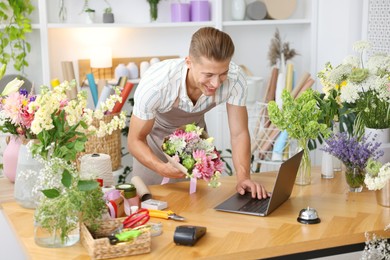 Photo of Professional florist with bouquet of flowers working at wooden table in shop