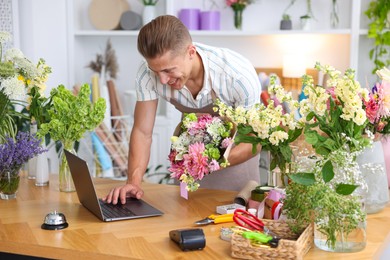 Photo of Professional florist with bouquet of flowers working at wooden table in shop