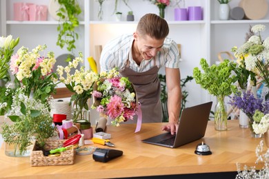 Photo of Professional florist with bouquet of flowers working at wooden table in shop