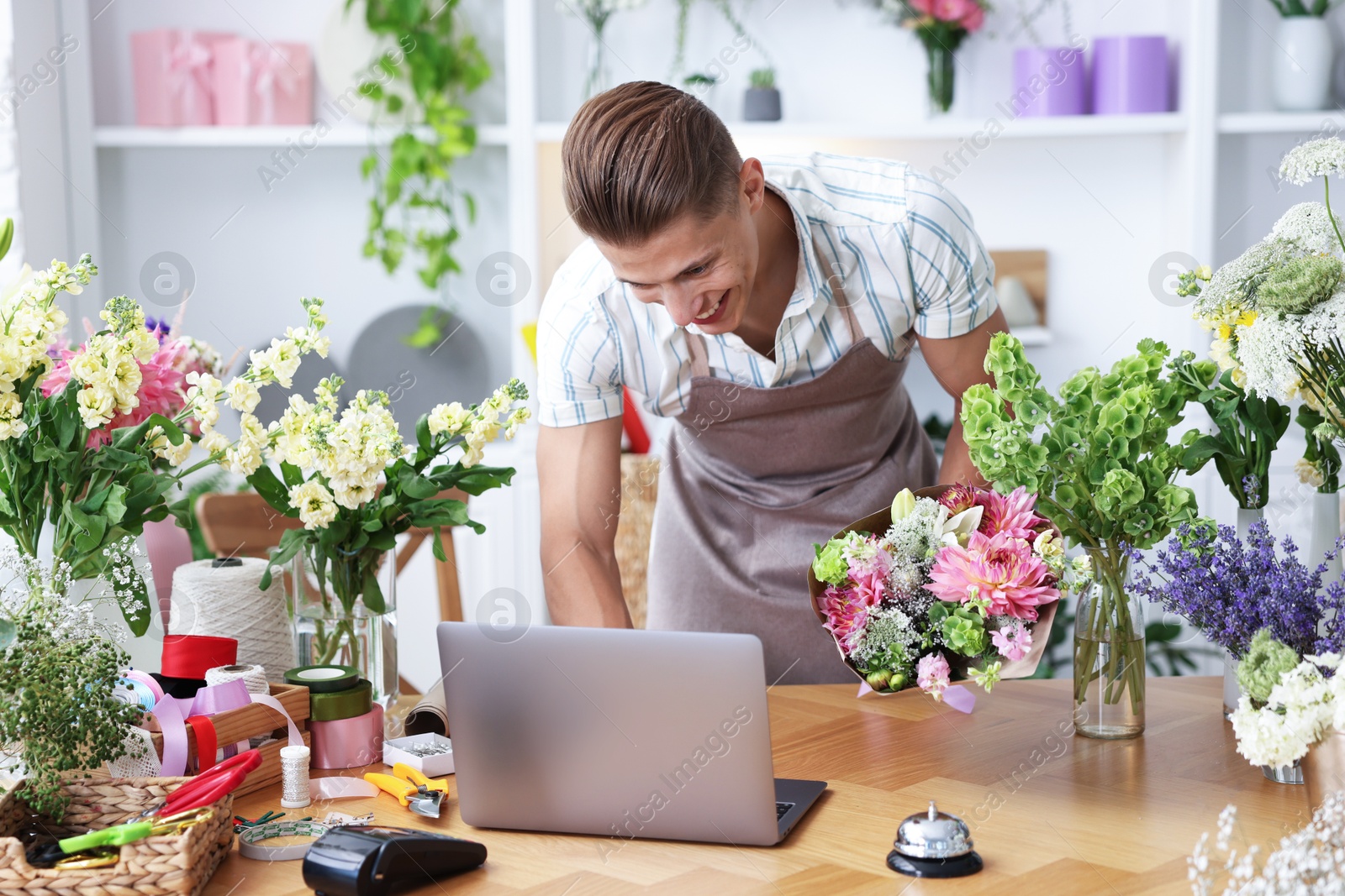 Photo of Professional florist with bouquet of flowers working at wooden table in shop