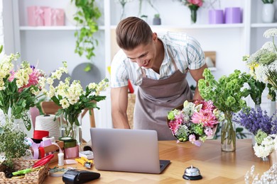 Photo of Professional florist with bouquet of flowers working at wooden table in shop