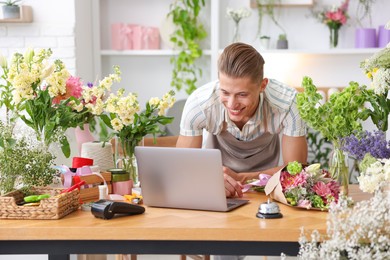 Photo of Professional florist with bouquet of flowers working at wooden table in shop