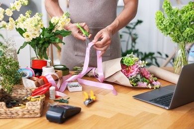 Photo of Professional florist making bouquet of flowers at wooden table in shop, closeup
