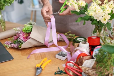 Photo of Professional florist making bouquet of flowers at wooden table in shop, closeup
