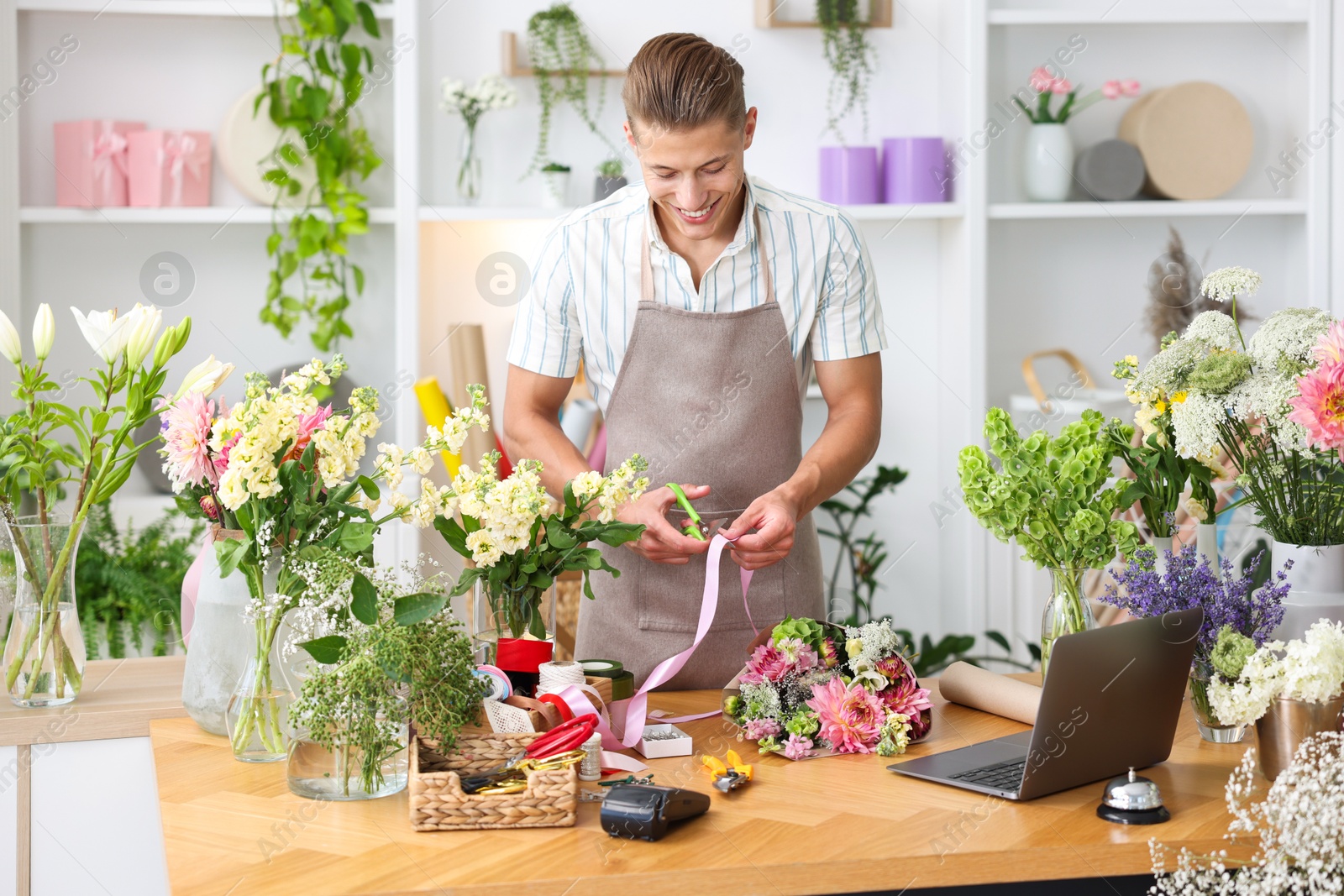Photo of Professional florist making bouquet of flowers at wooden table in shop