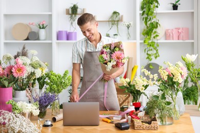 Photo of Professional florist making bouquet of flowers at wooden table in shop