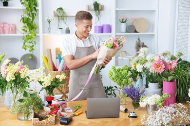 Photo of Professional florist making bouquet of flowers at wooden table in shop