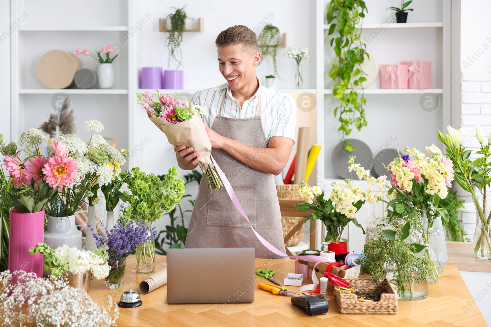 Photo of Professional florist making bouquet of flowers at wooden table in shop