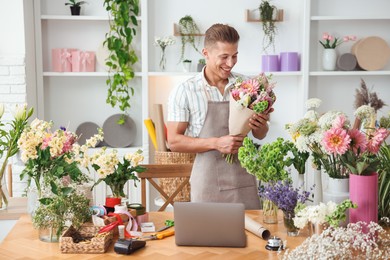 Photo of Professional florist making bouquet of flowers at wooden table in shop