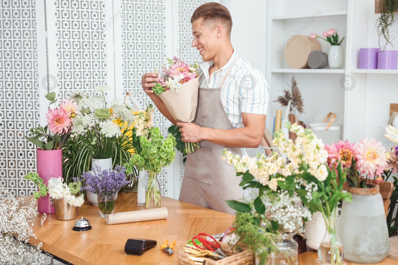 Photo of Professional florist making bouquet of flowers at wooden table in shop