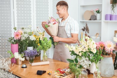 Photo of Professional florist making bouquet of flowers at wooden table in shop