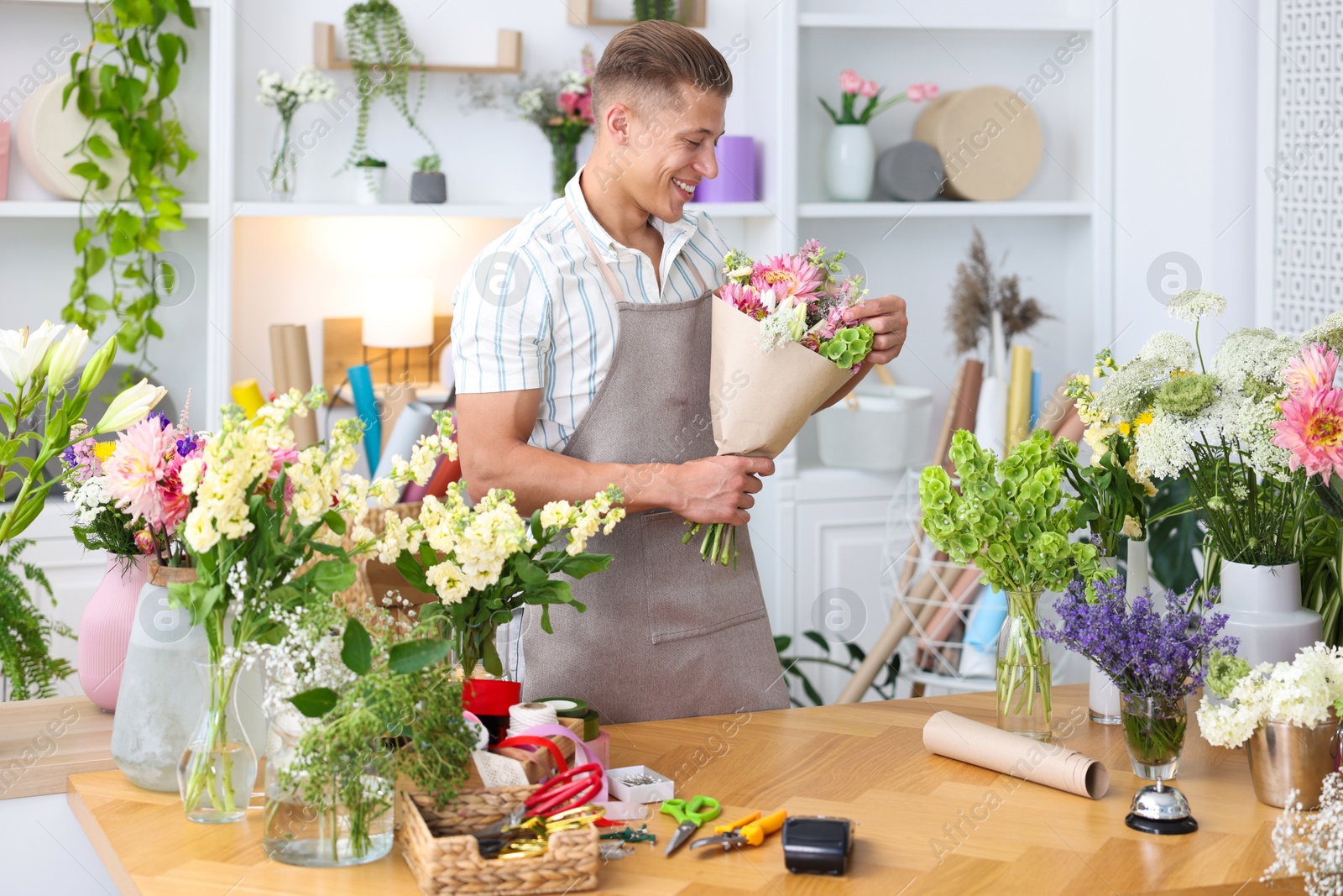 Photo of Professional florist making bouquet of flowers at wooden table in shop