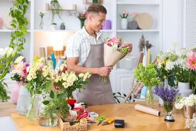 Photo of Professional florist making bouquet of flowers at wooden table in shop