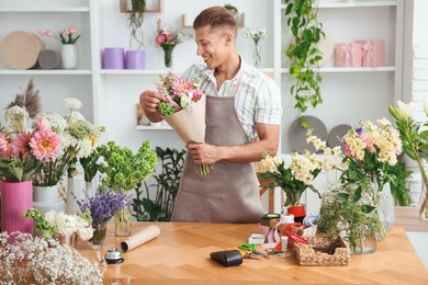 Photo of Professional florist making bouquet of flowers at wooden table in shop