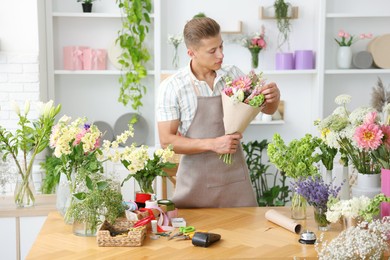 Photo of Professional florist making bouquet of flowers at wooden table in shop