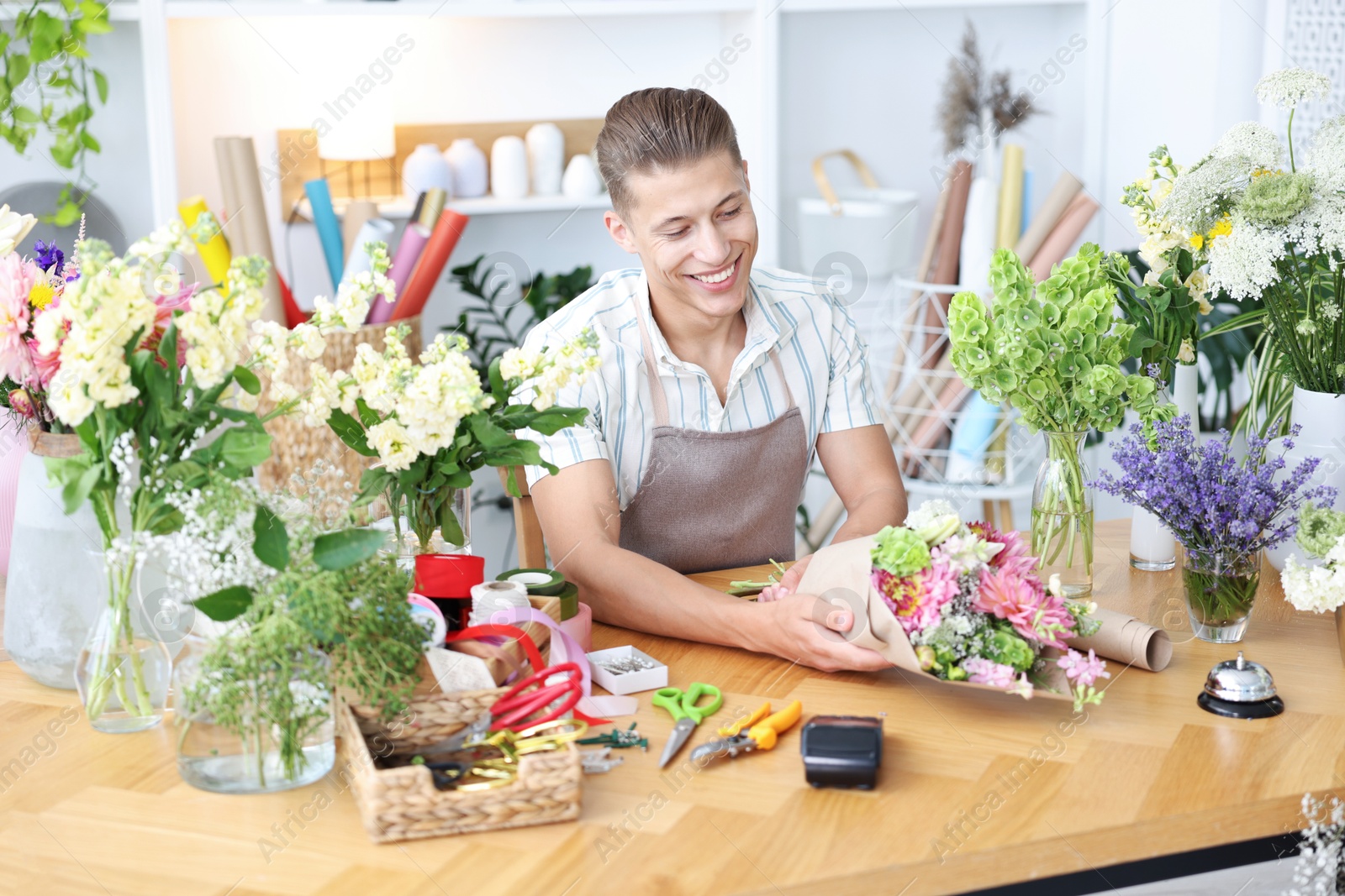 Photo of Professional florist making bouquet of flowers at wooden table in shop