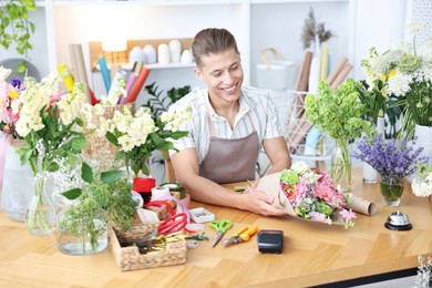 Photo of Professional florist making bouquet of flowers at wooden table in shop