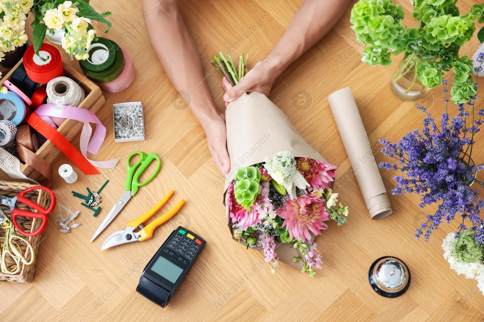 Photo of Professional florist making bouquet of flowers at wooden table, top view