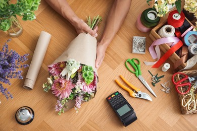 Photo of Professional florist making bouquet of flowers at wooden table, top view