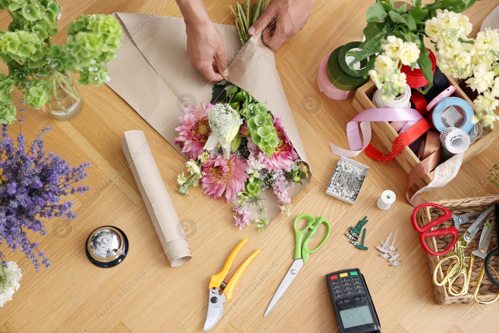 Photo of Professional florist making bouquet of flowers at wooden table, top view
