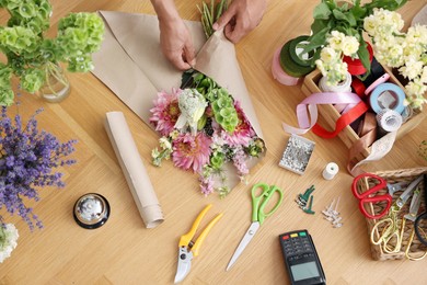 Photo of Professional florist making bouquet of flowers at wooden table, top view