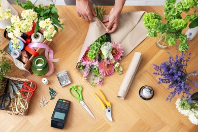 Photo of Professional florist making bouquet of flowers at wooden table, top view