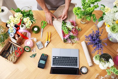 Photo of Professional florist making bouquet of flowers at wooden table, top view