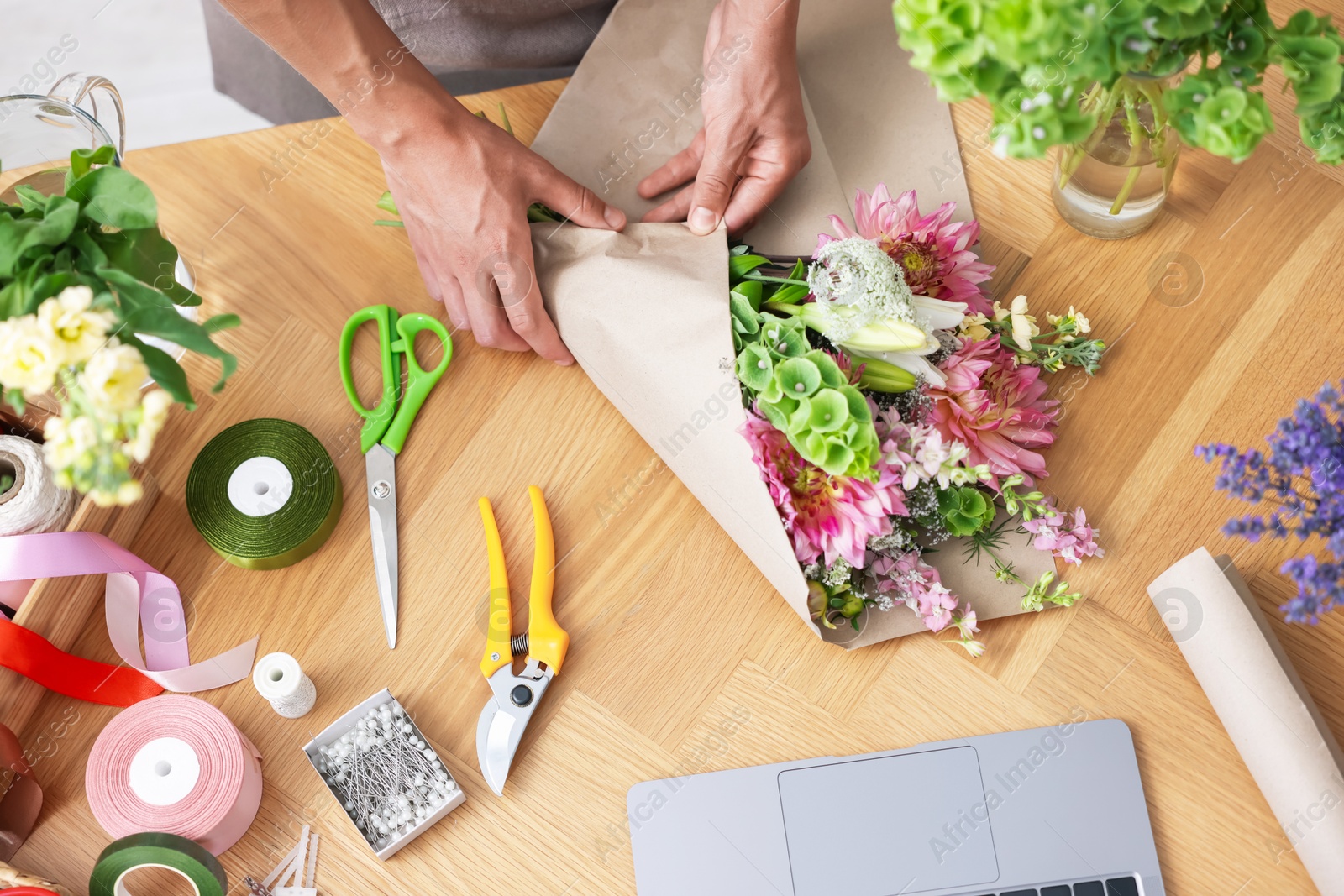 Photo of Professional florist making bouquet of flowers at wooden table, top view