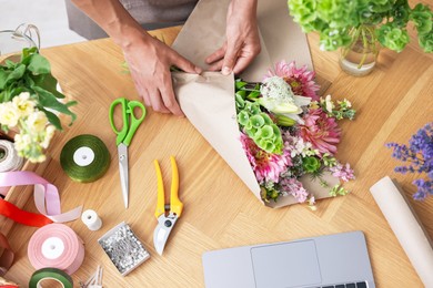 Photo of Professional florist making bouquet of flowers at wooden table, top view