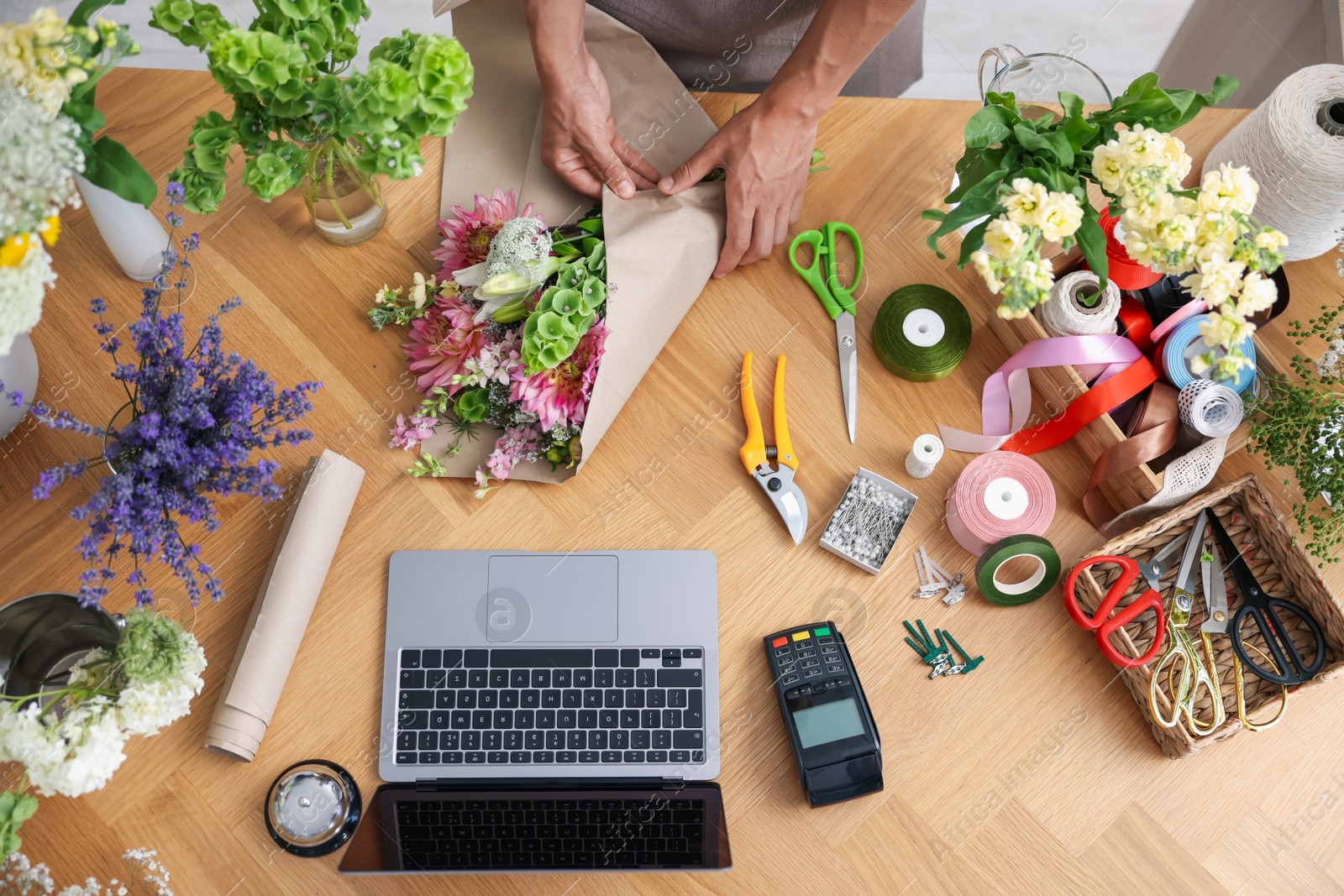 Photo of Professional florist making bouquet of flowers at wooden table, top view