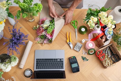 Photo of Professional florist making bouquet of flowers at wooden table, top view