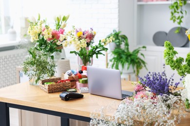 Photo of Laptop, beautiful flowers, scissors and other tools on wooden table in florist's shop