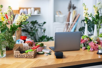 Photo of Laptop, beautiful flowers, scissors and other tools on wooden table in florist's shop