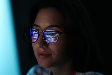 Photo of Young woman wearing glasses with reflection on dark background, closeup