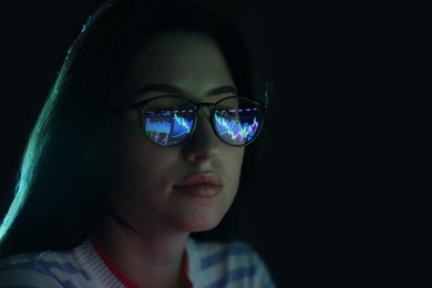 Photo of Young woman wearing glasses with reflection on dark background, closeup