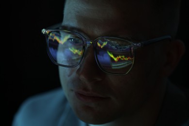 Photo of Young man wearing glasses with reflection on dark background, closeup