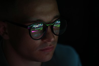 Photo of Young man wearing glasses with reflection on dark background, closeup