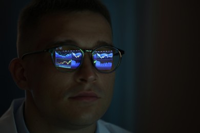Photo of Young man wearing glasses with reflection on dark background, closeup