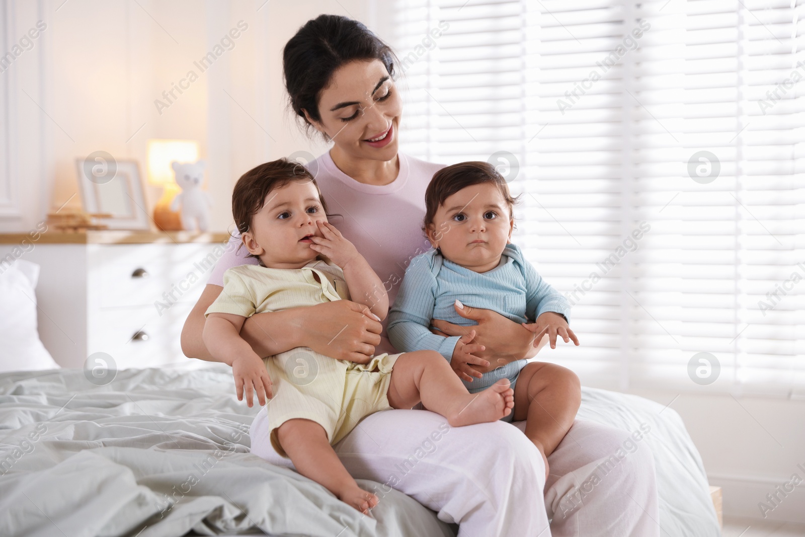 Happy mother with her cute little twin babies on bed indoors Photo of Happy mother with her cute little twin babies on bed indoors