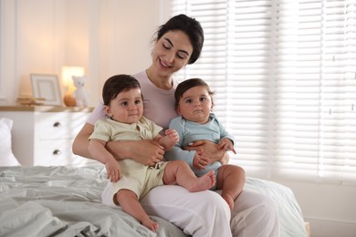 Photo of Happy mother with her cute little twin babies on bed indoors