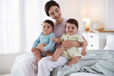 Photo of Happy mother with her cute little twin babies on bed indoors