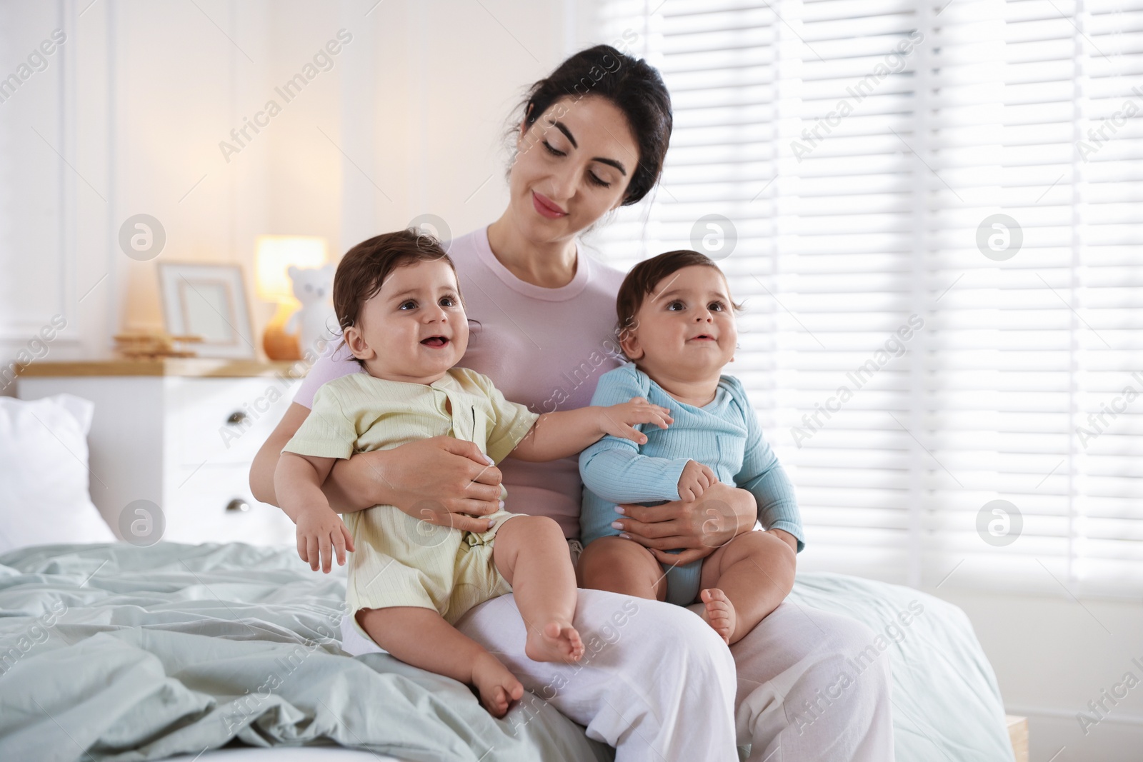 Photo of Mother with her cute little twin babies on bed indoors