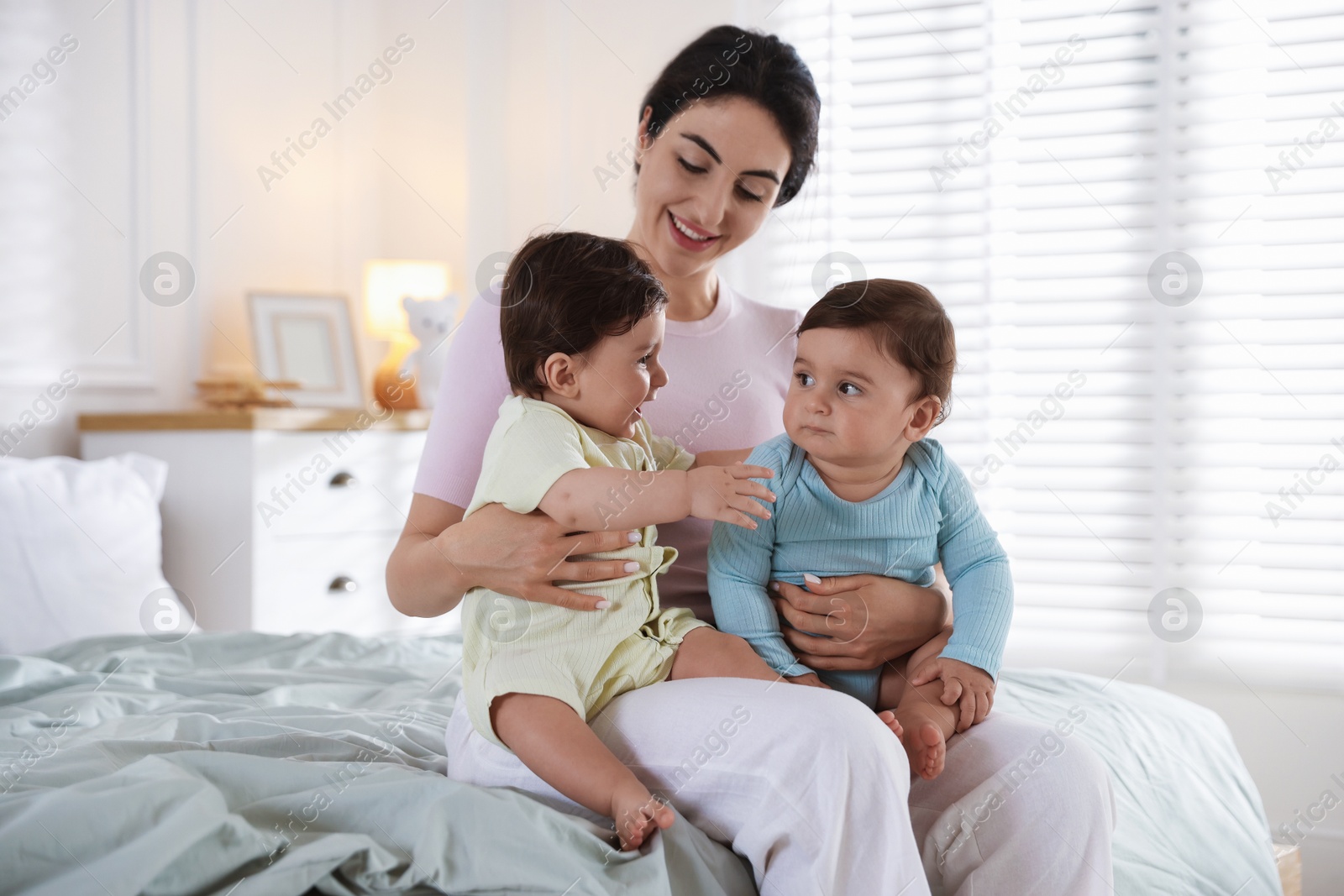 Photo of Happy mother with her cute little twin babies on bed indoors