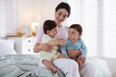 Photo of Happy mother with her cute little twin babies on bed indoors